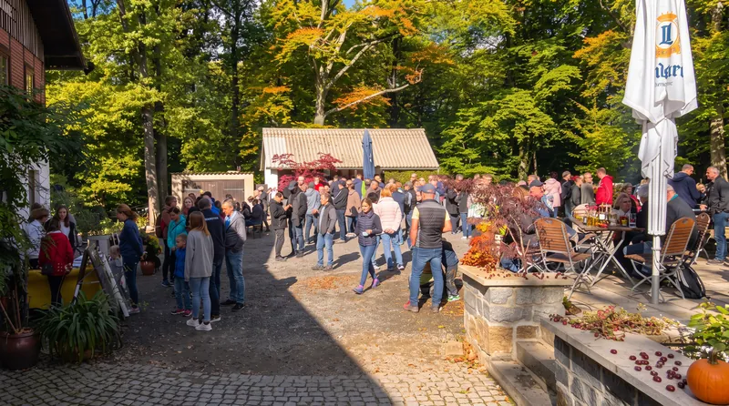 Gäste am Kiosk der Hochsteinbaude: Andrang am Ausgabefenster, Biertische und herbstlich geschmückte Mauer im Hof
