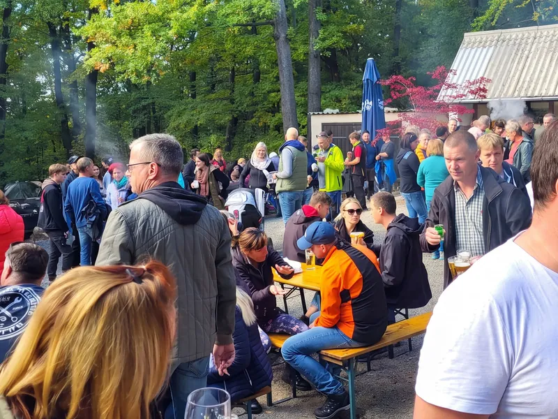 Hochsteinkirmes: Gäste mit Bier und Essen an Biertischen vor dem Kiosk, Rauch vom Grill, dahinter der herbstliche Buchenwald